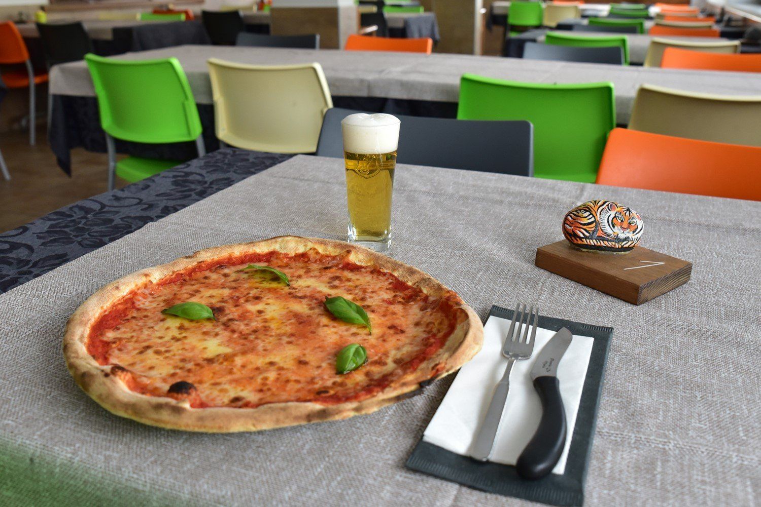 Pizza margherita apparecchiata con posate e una birra
