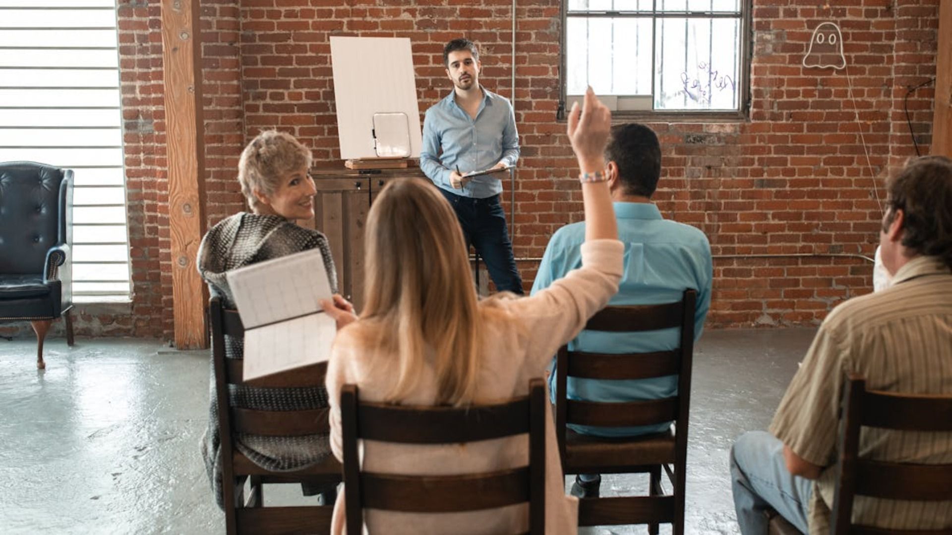 Un grupo de personas están sentadas en sillas y una mujer levanta la mano para responder una pregunta.