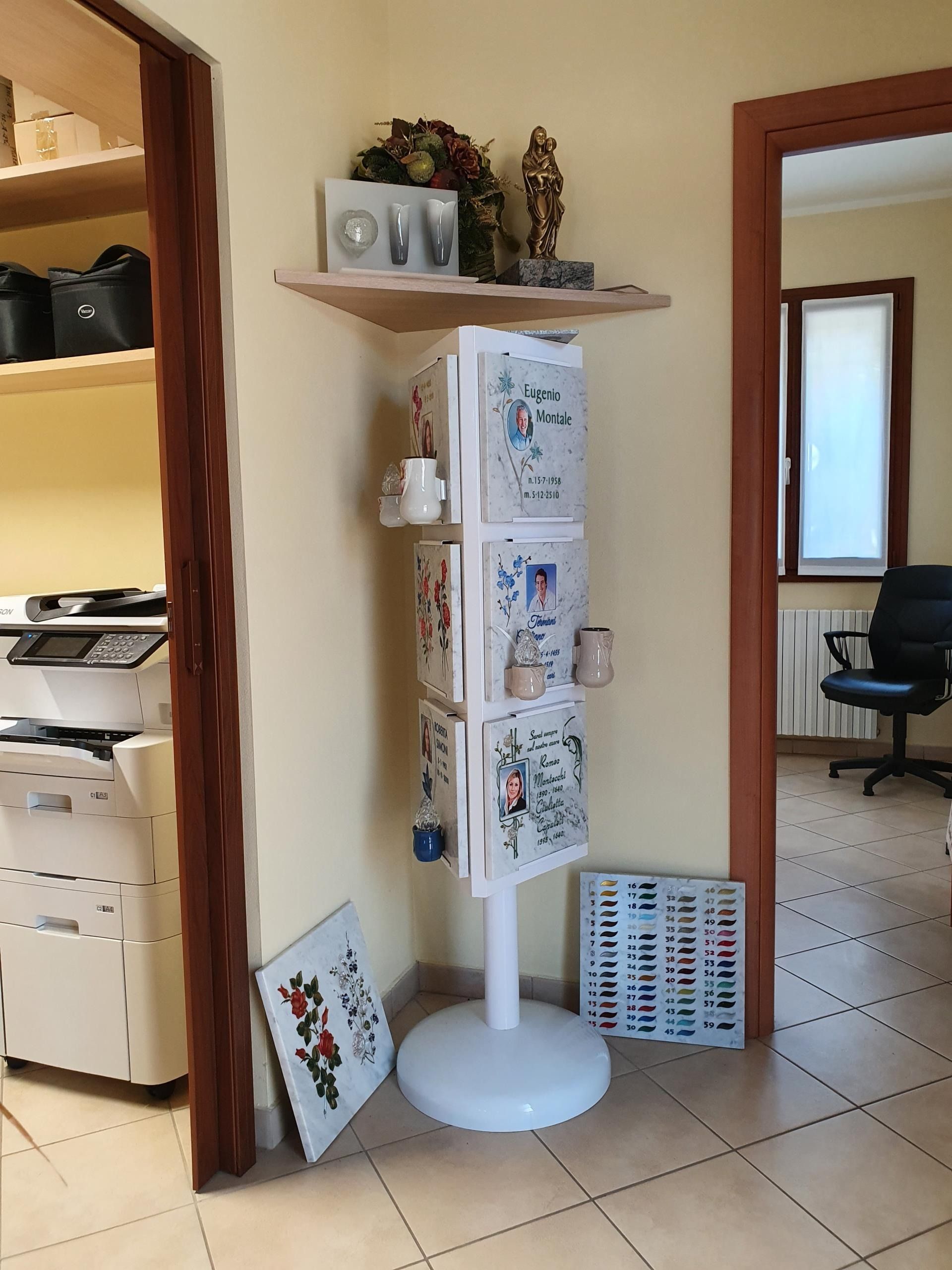 Un espositore angolare a pavimento, posizionato tra la sala stampanti e un ufficio con scrivania, contiene opuscoli promozionali.