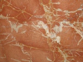 Primo piano di marmo color terracotta con evidenti venature bianche e oro pallido che attraversano tutta la pietra.