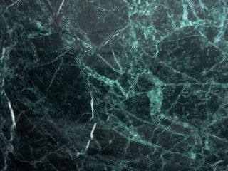 Una trama di marmo verde smeraldo scuro con intricate venature ramificate bianche e verde chiaro.