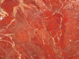 Primo piano di una lastra di pietra rossa con intricate venature bianche e marroni che percorrono tutta la superficie.