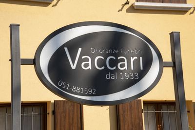 Insegna ovale dell'impresa di pompe funebri Vaccari, fondata nel 1933, con numero di telefono, montata su una cornice nera.