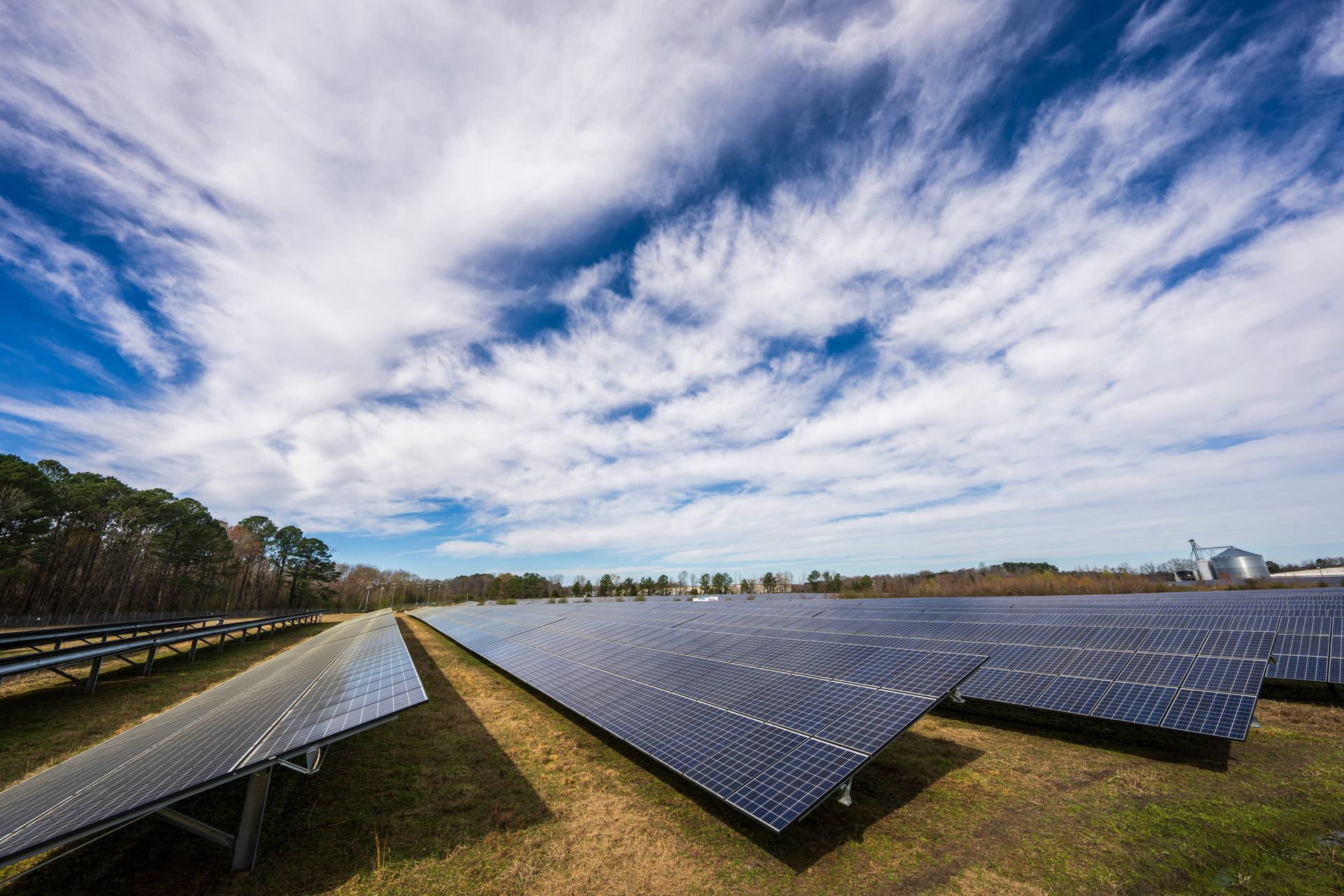 A field of solar panels under a cloudy blue sky.