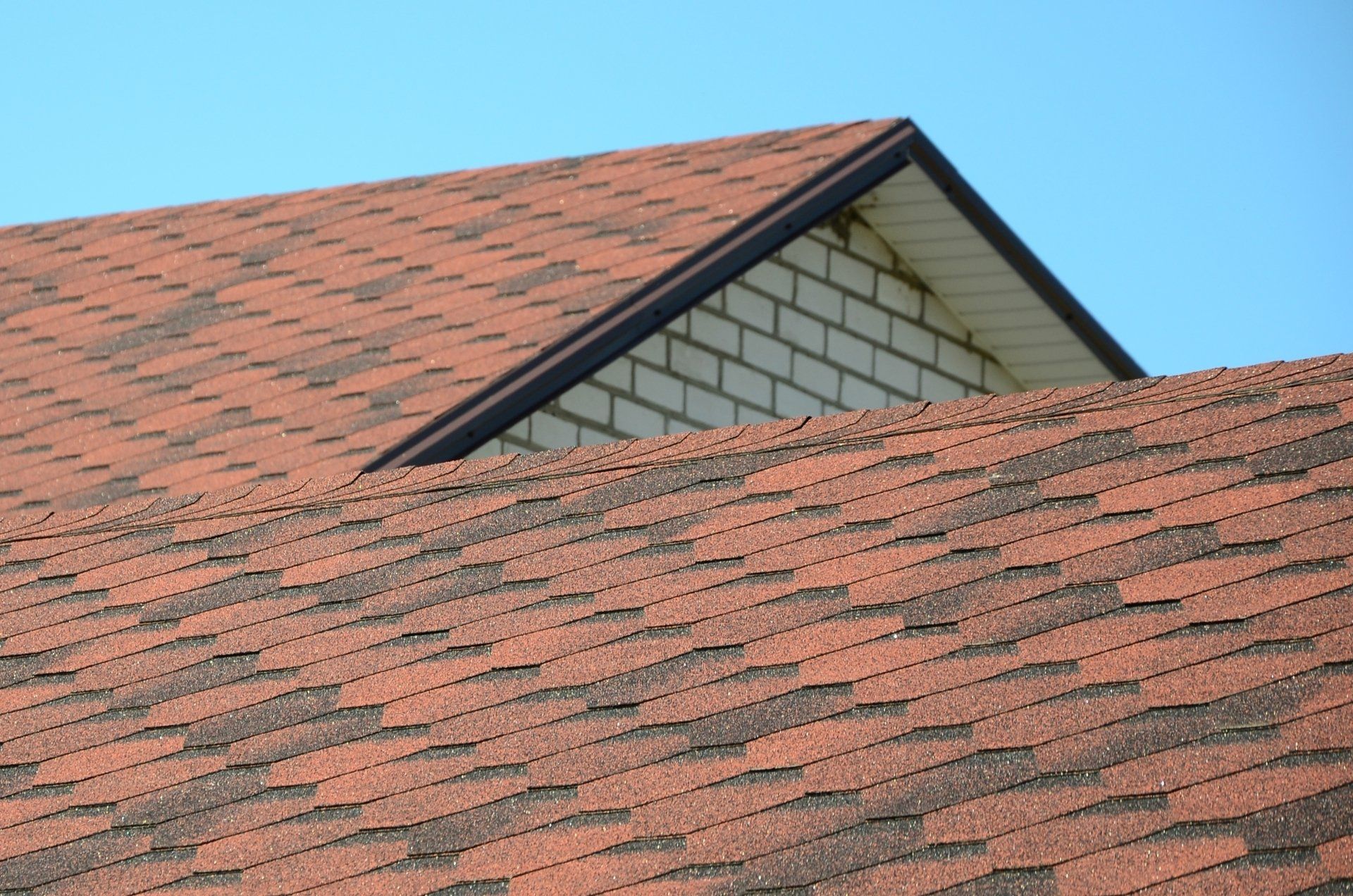 A close up of a red roof with a brick building in the background.