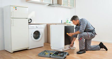 A man is fixing a refrigerator in a kitchen.
