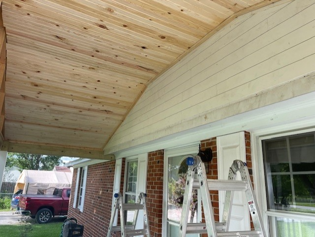 Wooden porch ceiling under construction, with ladders and a brick house visible. Wooden porch ceiling under construction, with ladders and a brick house visible.