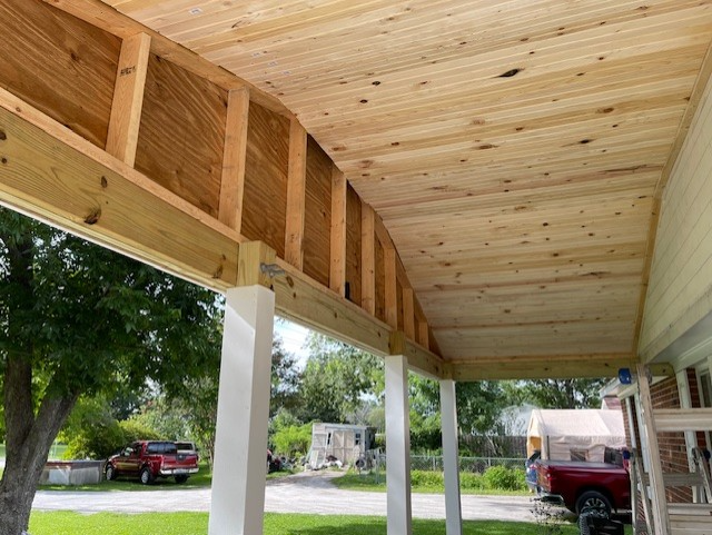 Porch ceiling with wood planks, beams and white columns; view to the outside.
