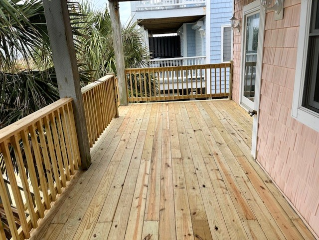 Wooden deck with railing on a building; view of another building in background.
