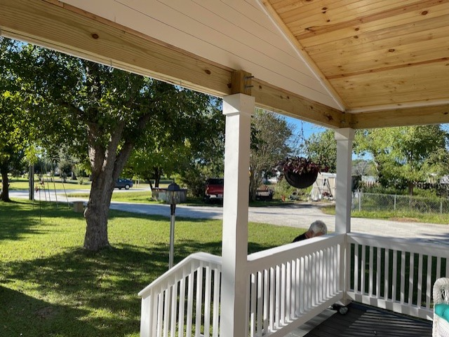 A porch with white railing and columns overlooks a green yard and street.