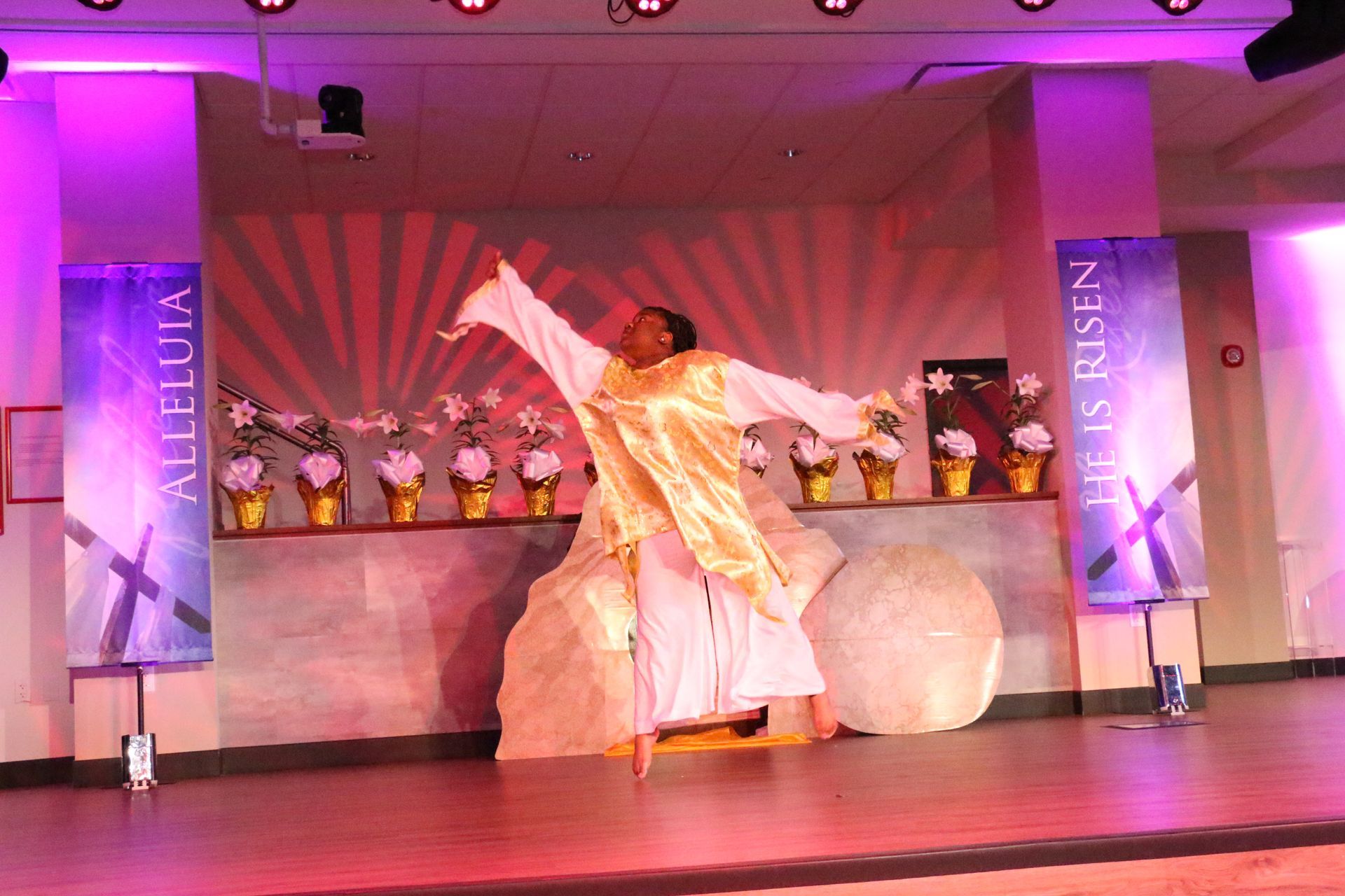 A man in a white robe is standing on a stage in front of a sign that says alleluia