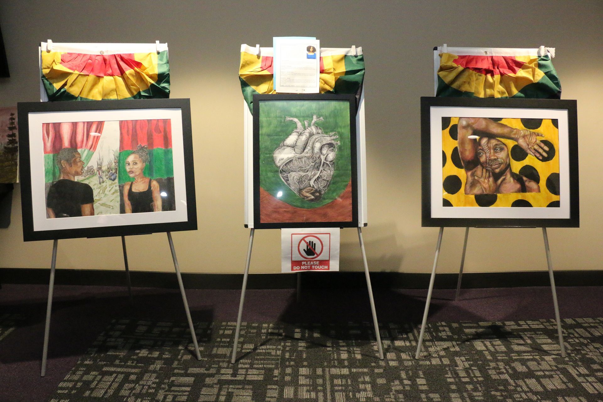 Three paintings are displayed on easels in a room