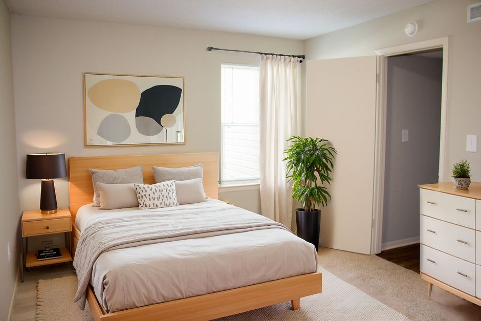 A bedroom with a bed , dresser , lamp , and window.