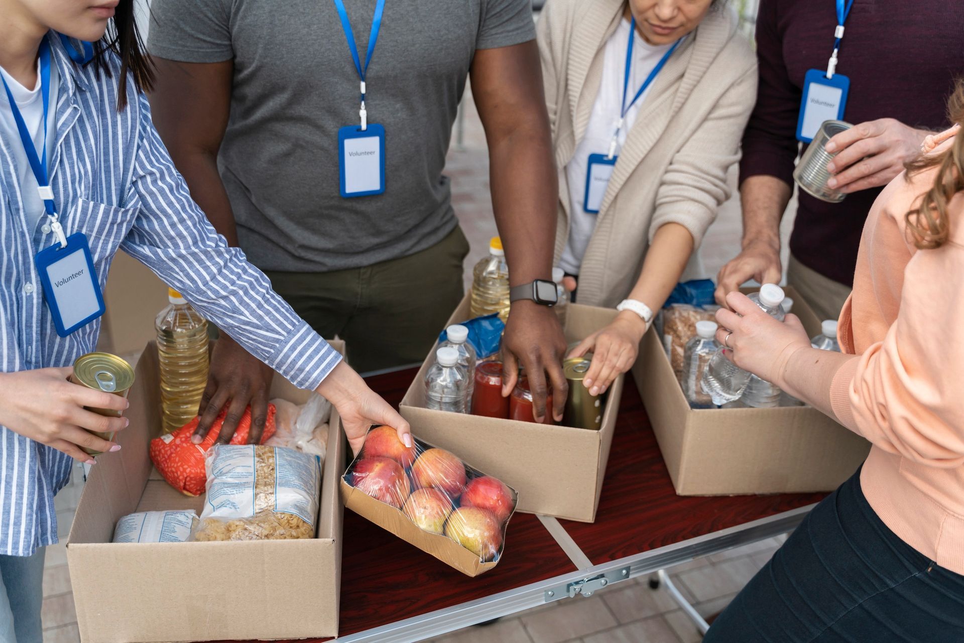 Volunteers with name tags packing food items into cardboard boxes on a table.