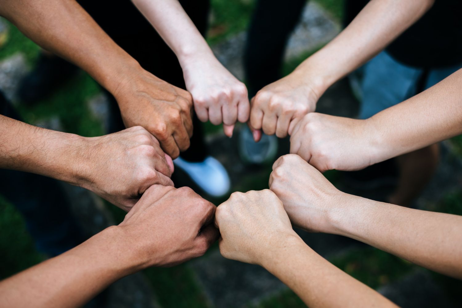 A group of people standing in a circle, their fists joined together in the center to symbolize unity and teamwork.