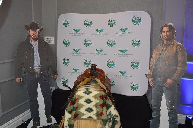 Two life-sized cardboard cutouts of men in western wear stand on either side of a saddle resting on a display backdrop.