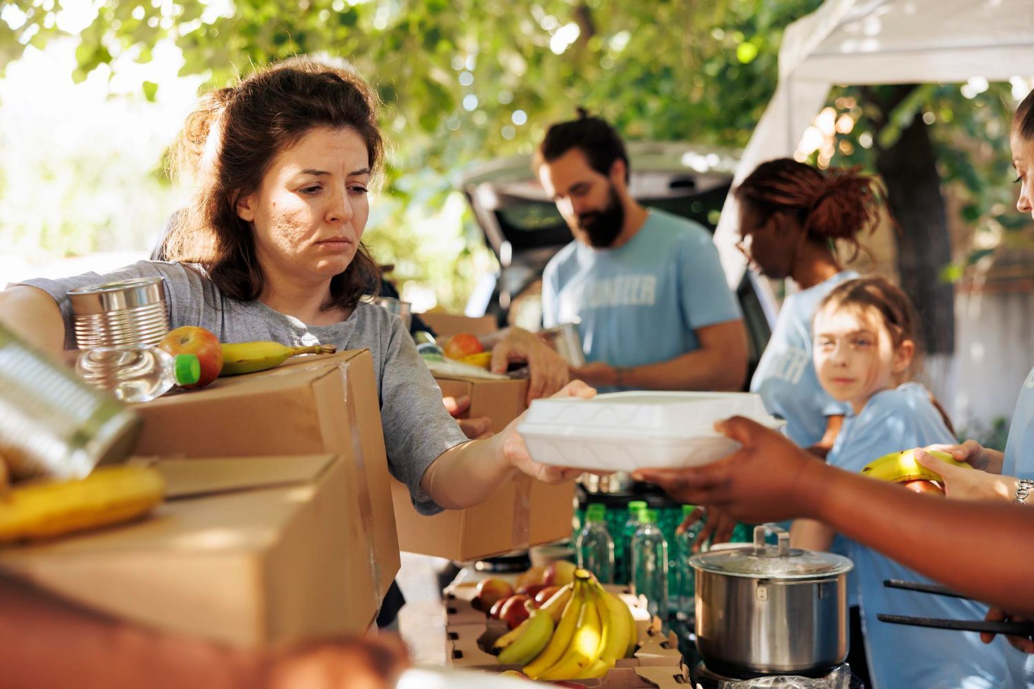 Volunteers distribute meals and boxes of food at an outdoor community event.