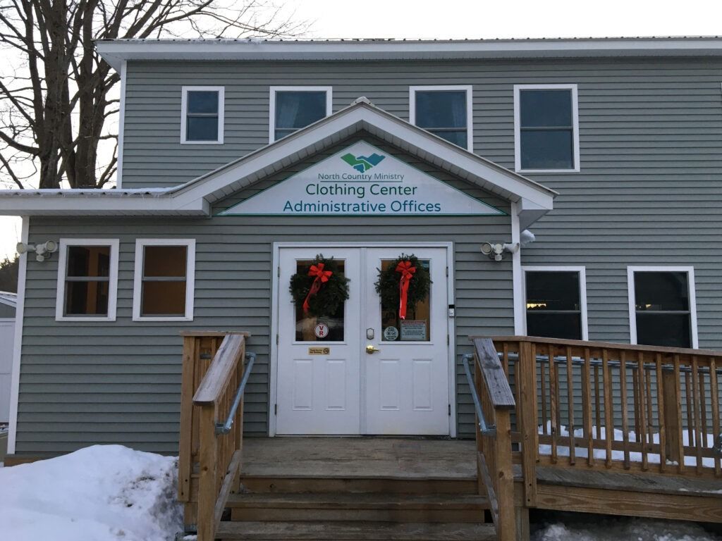 Gray building exterior with a white door, signage for Clothing Center Administrative Offices, and stairs in the snow.