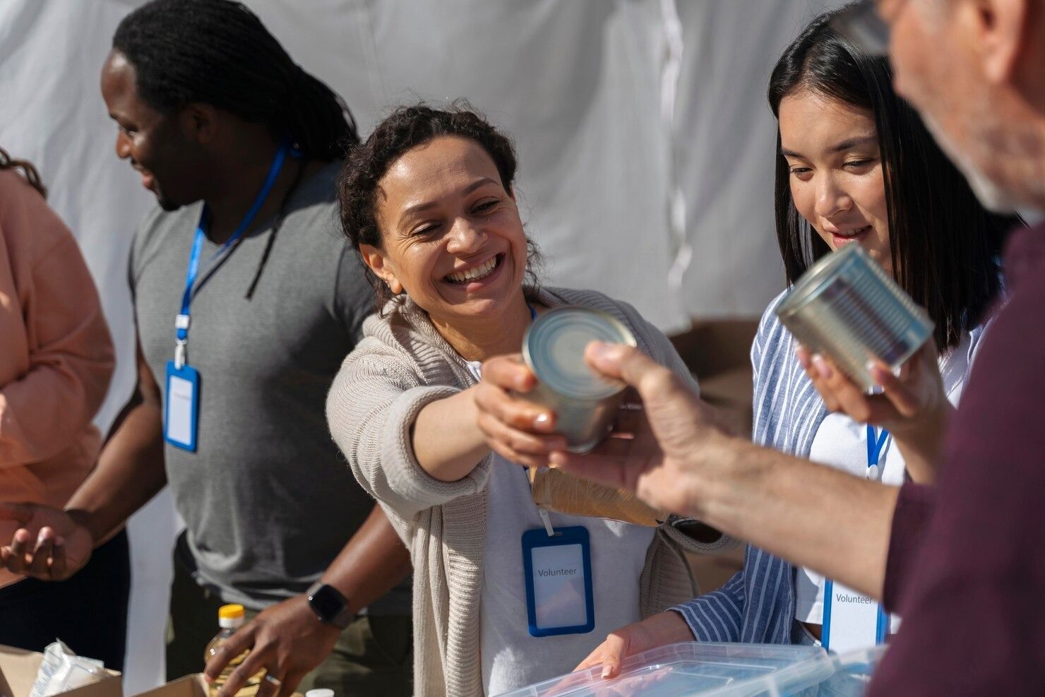 Volunteers at an outdoor food bank distribute canned goods to individuals.