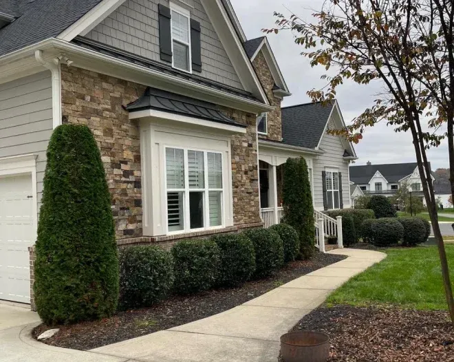 A house with a walkway leading to it and bushes in front of it.