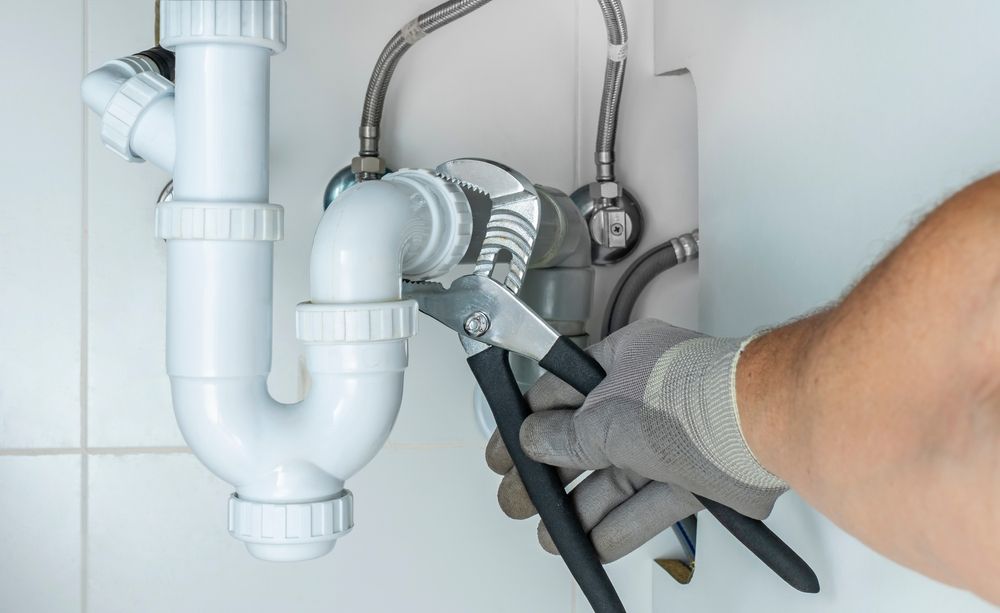 Plumber using a wrench to fix under-sink white PVC pipes