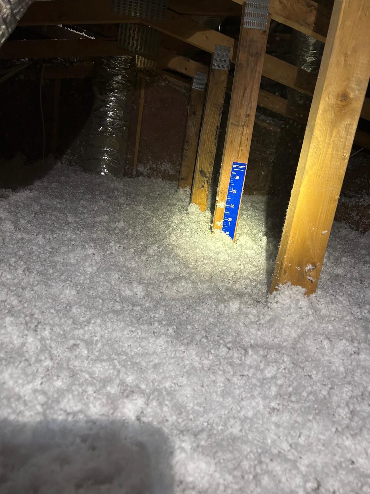 Person in protective suit sprays pink foam insulation onto a wooden wall.