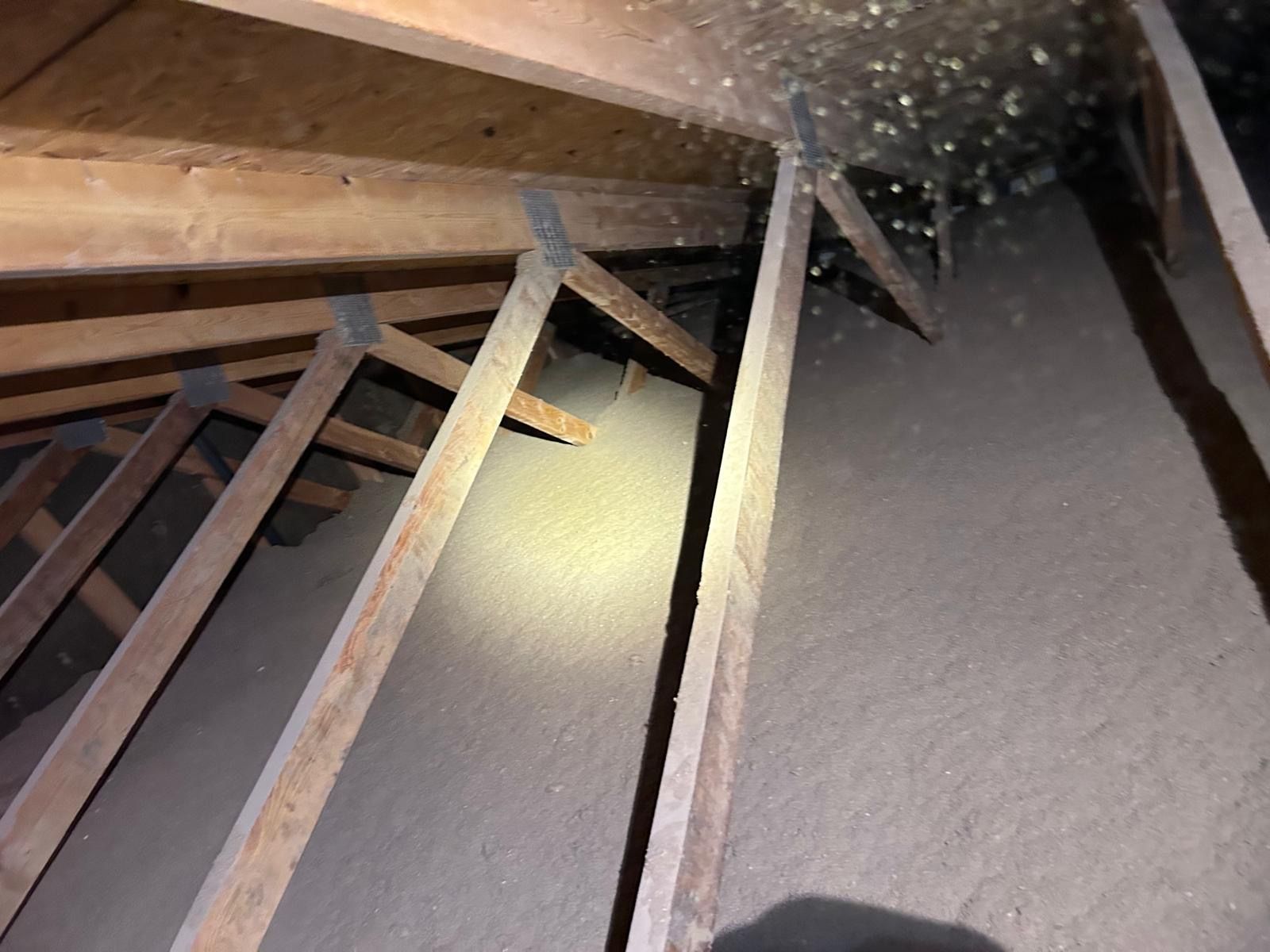 Pink insulation fills an attic with wooden beams and a central walkway.