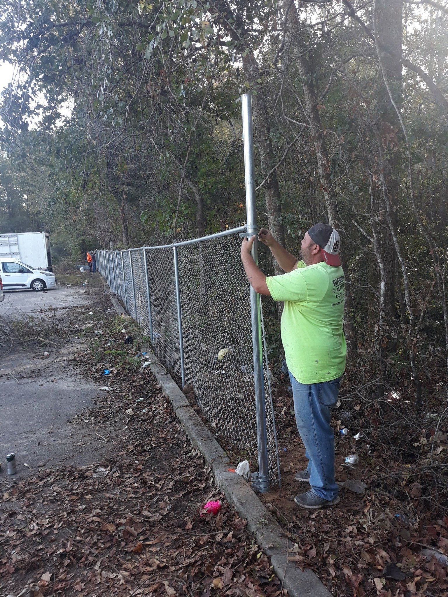 A man is working on a chain link fence in the woods.
