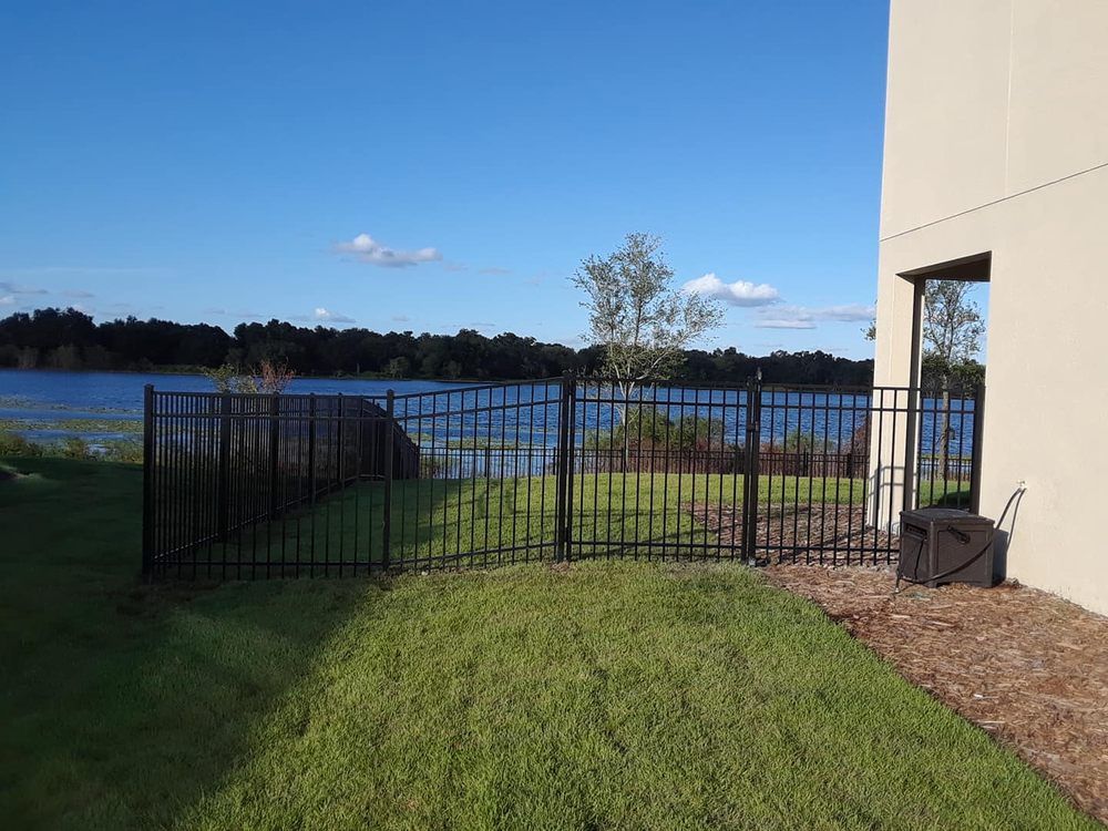 A black fence surrounds a yard with a lake in the background.