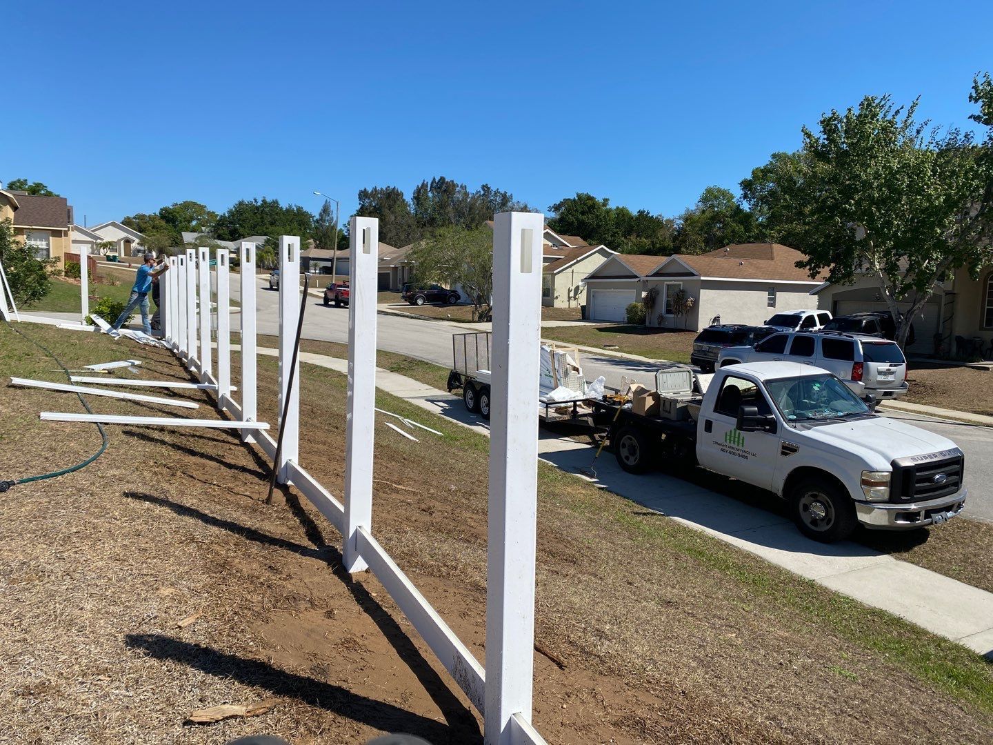 A white truck is parked on the side of the road next to a fence.