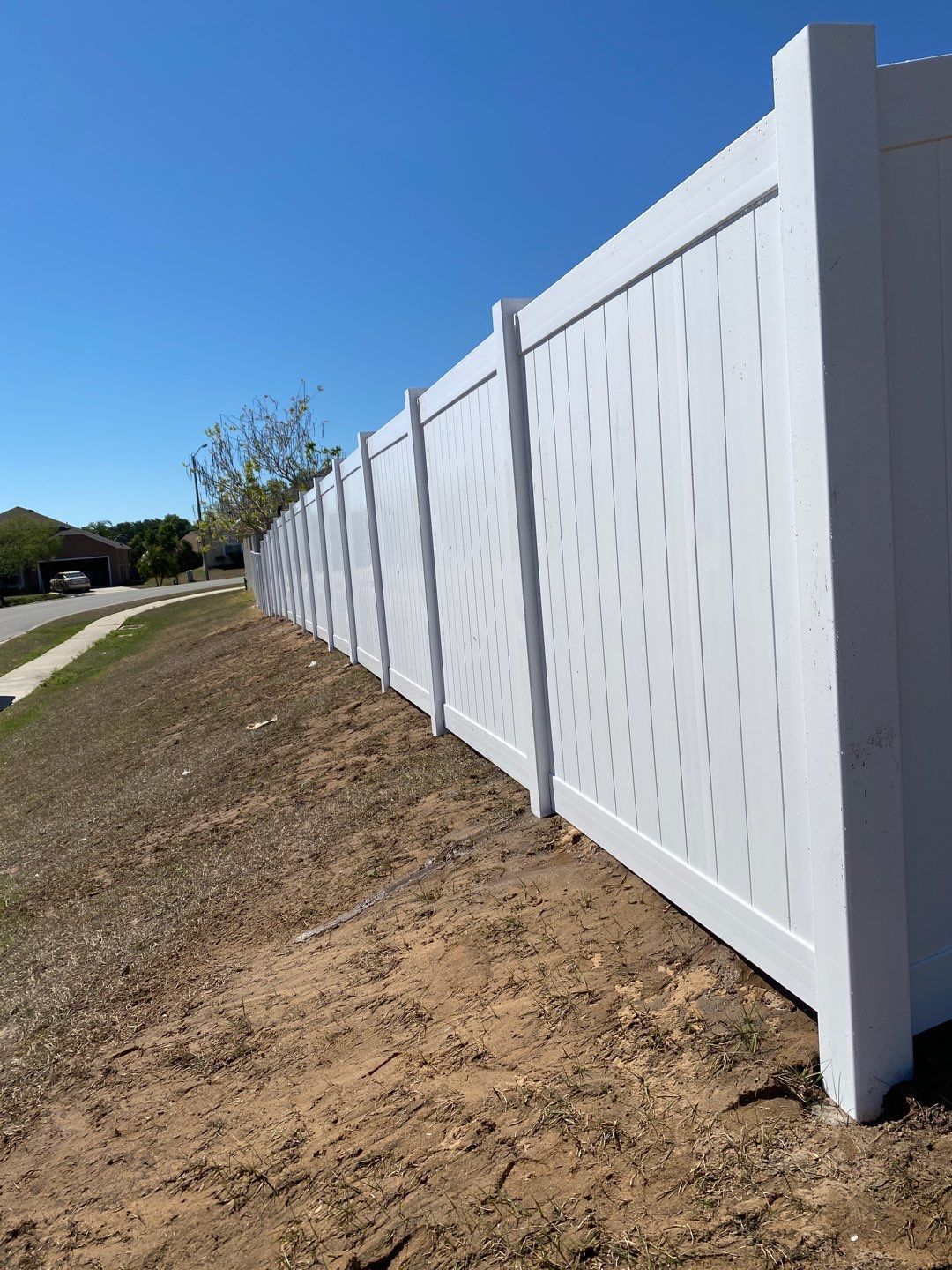 A white fence is sitting on top of a dirt hill next to a road.