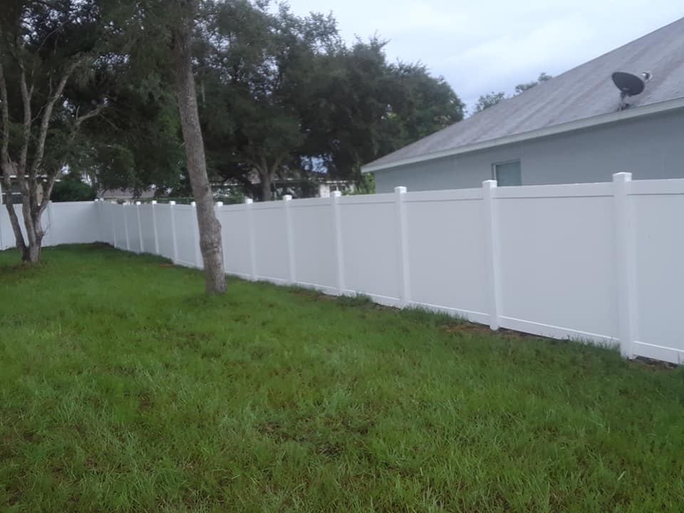 A white fence surrounds a lush green yard in front of a house.