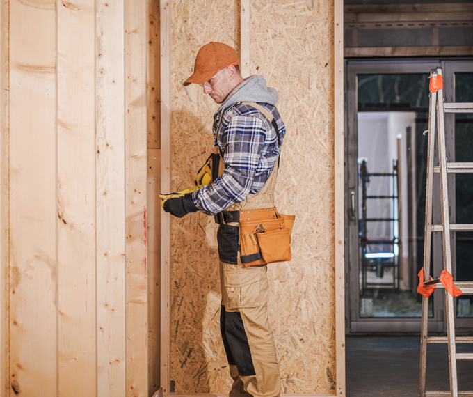 A man is measuring a piece of wood with a tape measure.