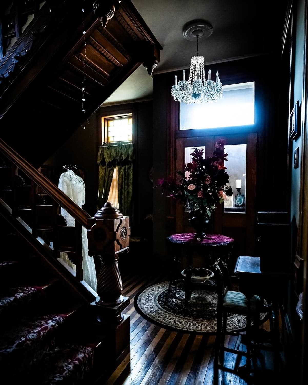 A dark hallway with stairs and a chandelier hanging from the ceiling