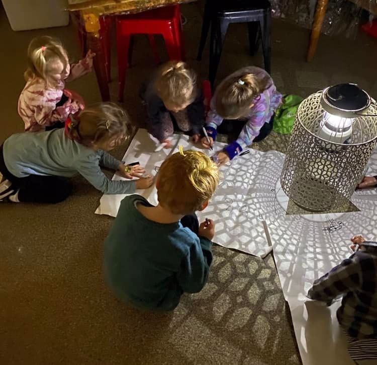 A child sits on a carpeted floor, playing with a wooden train on a track that leads through a teal block archway.