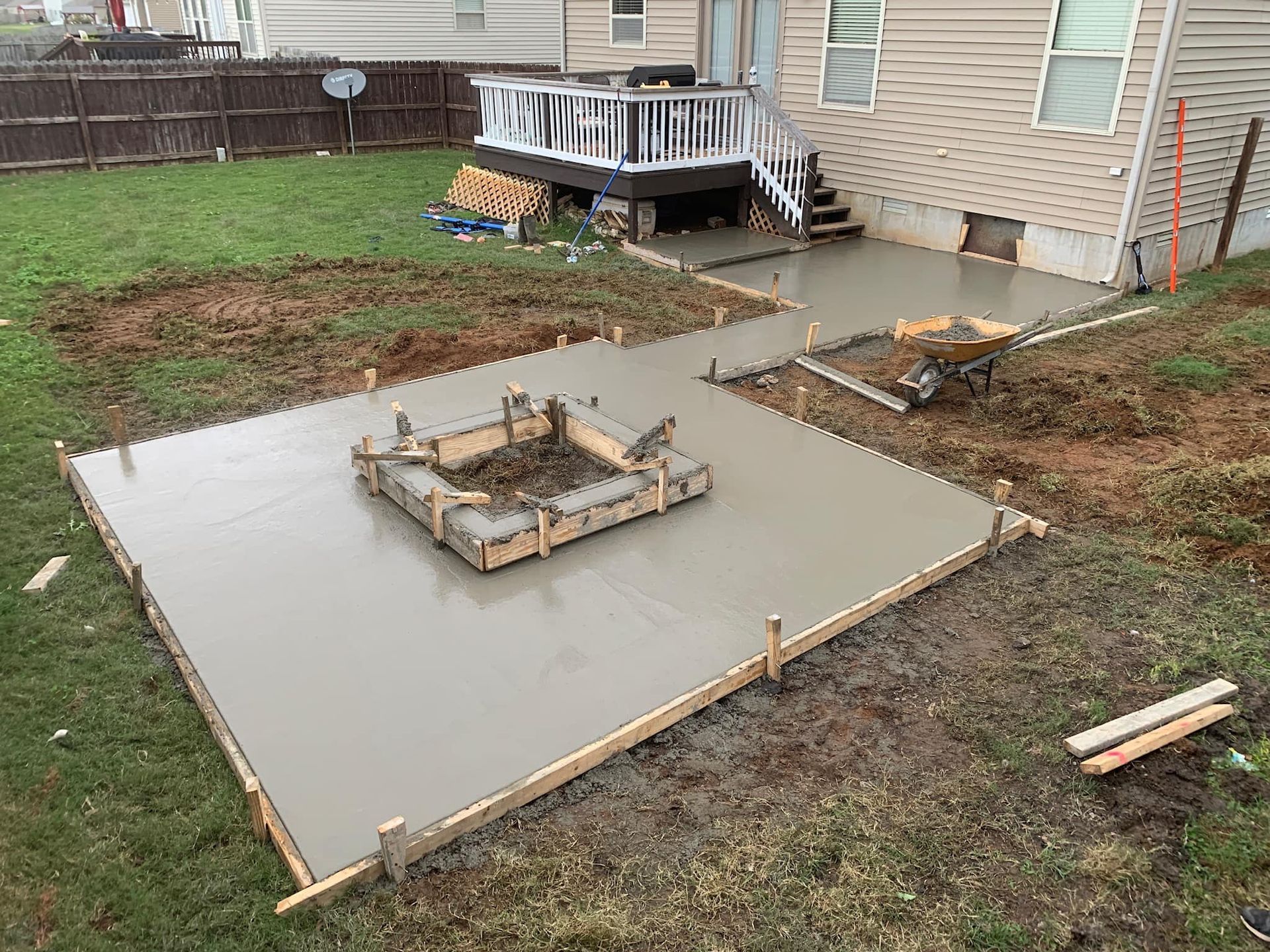 Freshly poured concrete patio with fire pit form, next to a house and deck.
