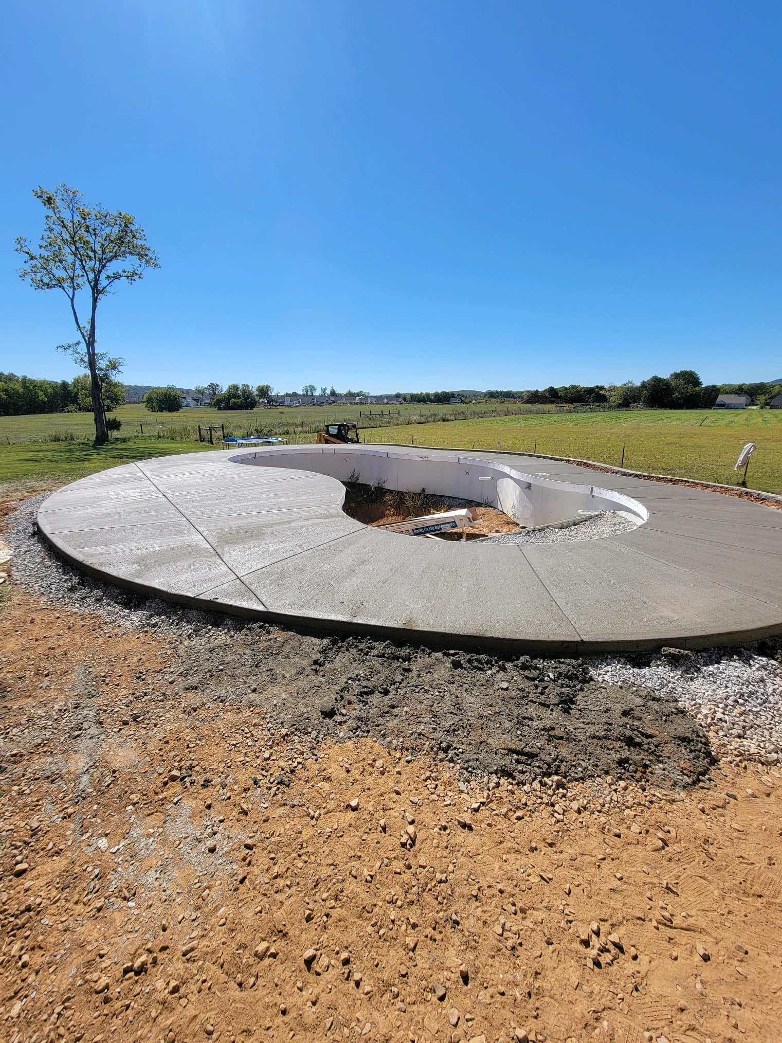 Circular concrete structure in a rural setting; dirt ground, blue sky, and small tree visible.