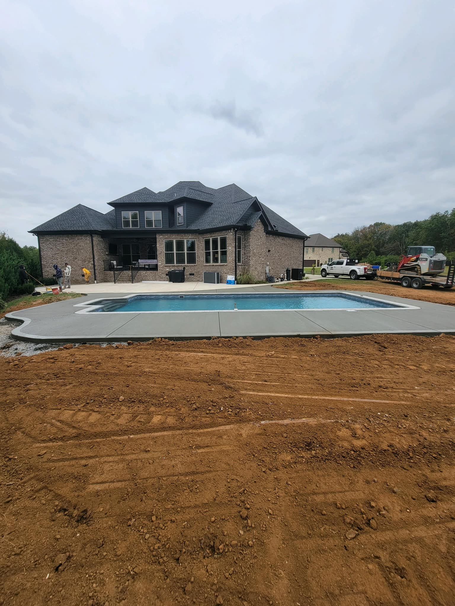 Backyard with a pool in front of a two-story brick house on an overcast day.