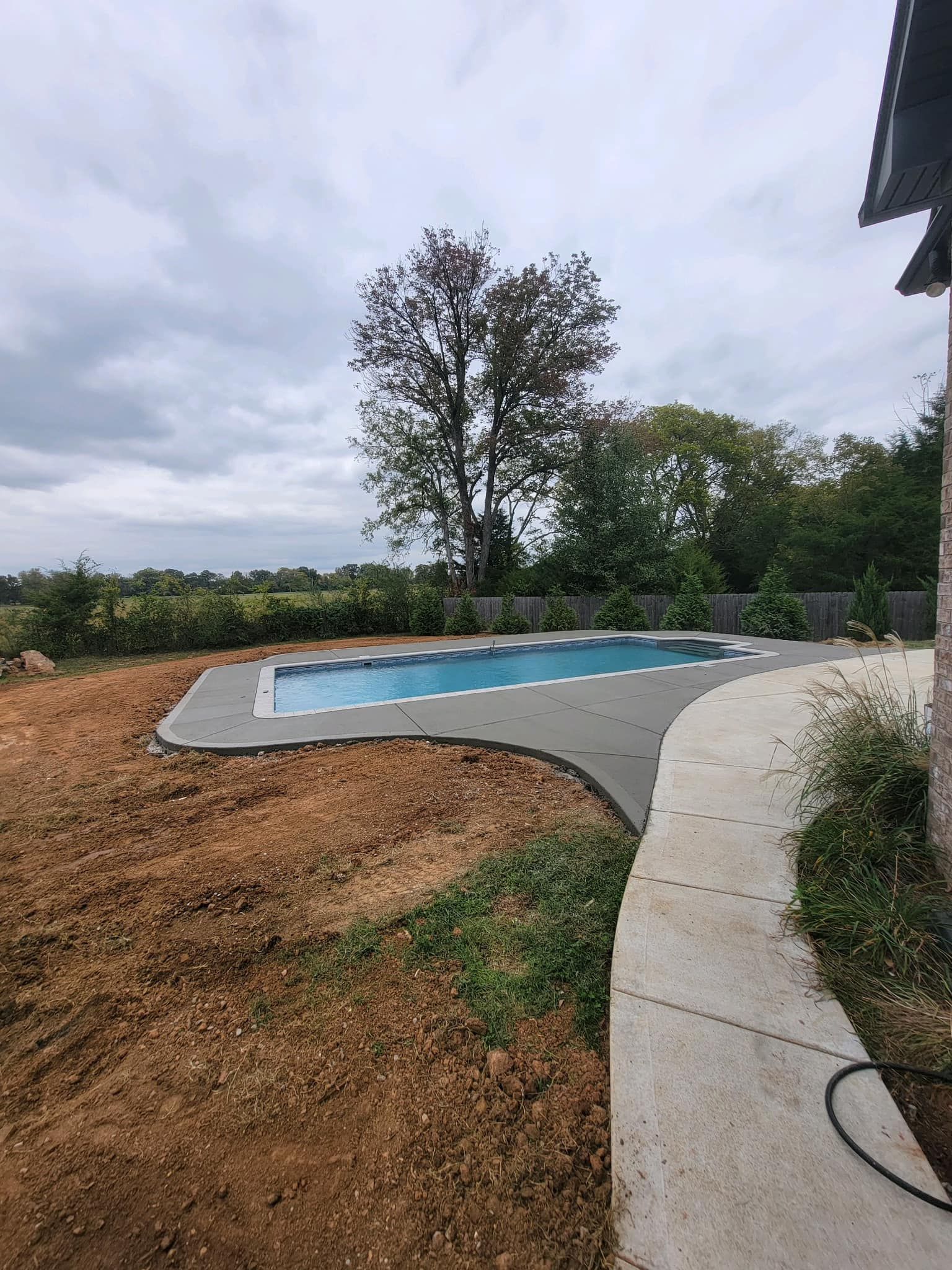 A backyard with a newly constructed pool surrounded by concrete; cloudy sky above.