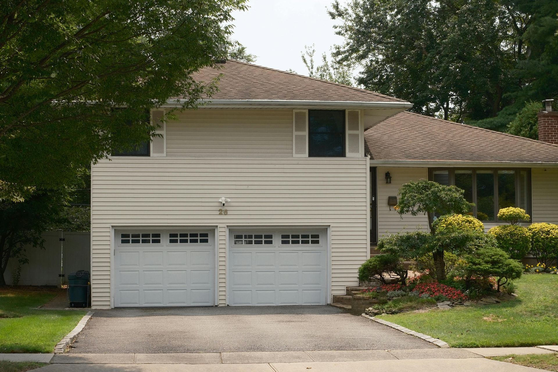 Two-story beige house with two-car garage, driveway, and landscaping.