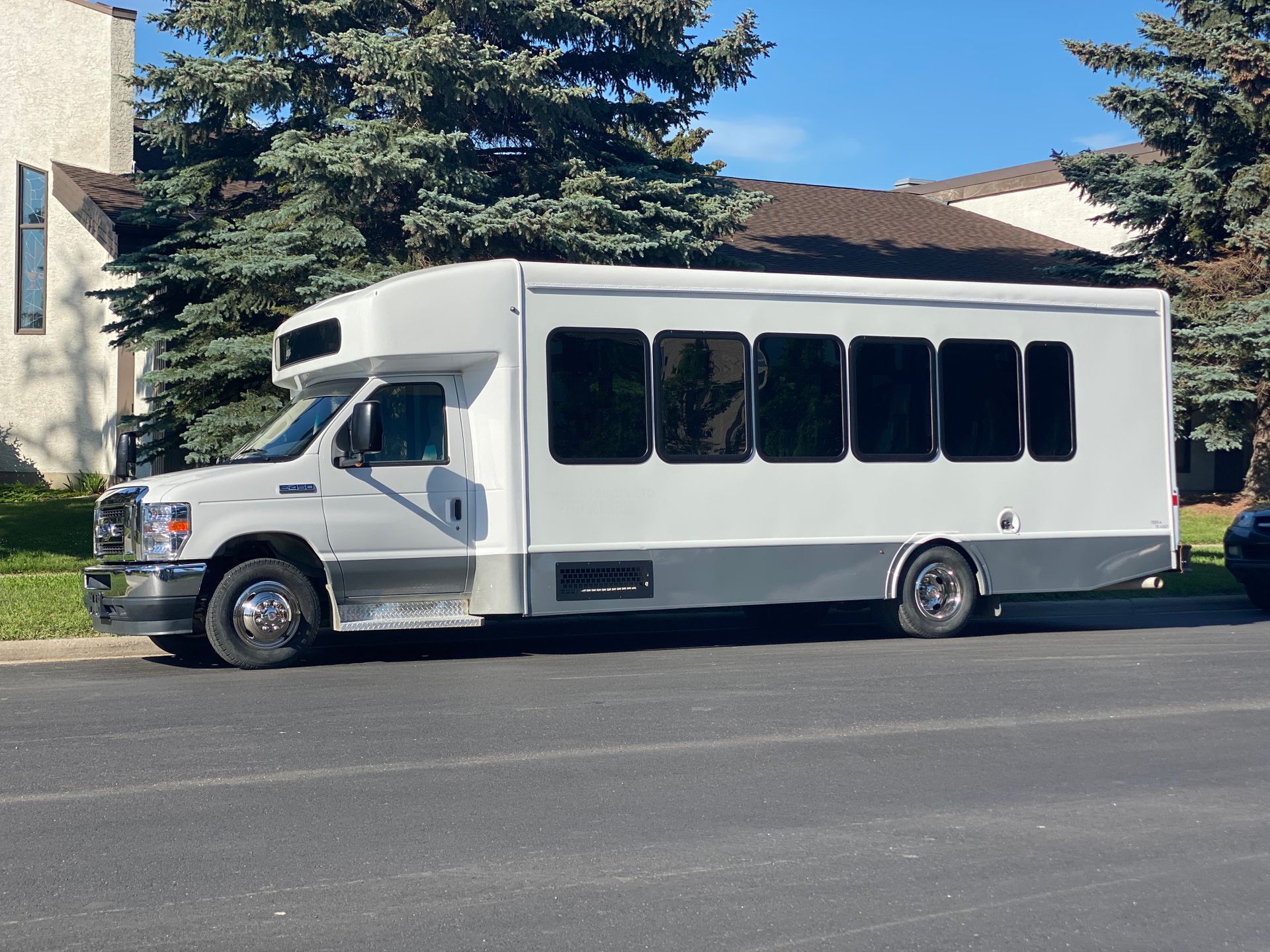 a white 24 passenger executive shuttle bus is parked on the side of the road .
