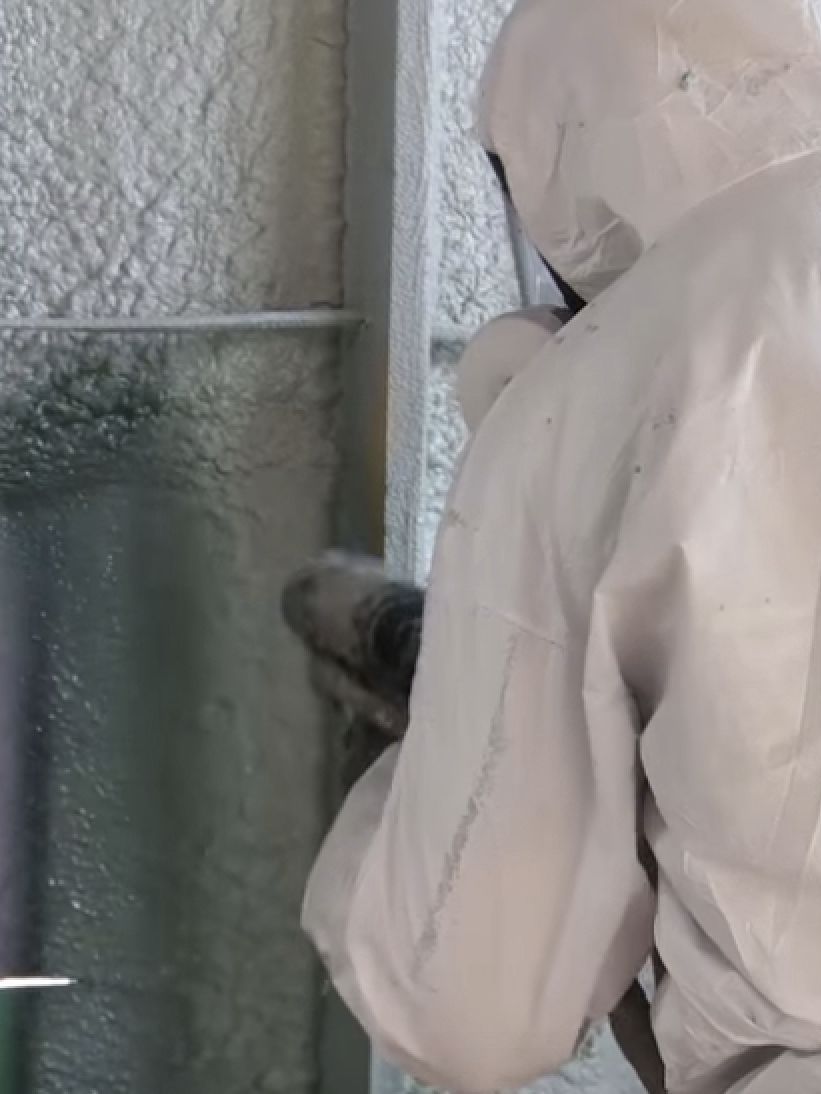 A man in a protective suit is spraying Mineral Wool Insulation on a wall.