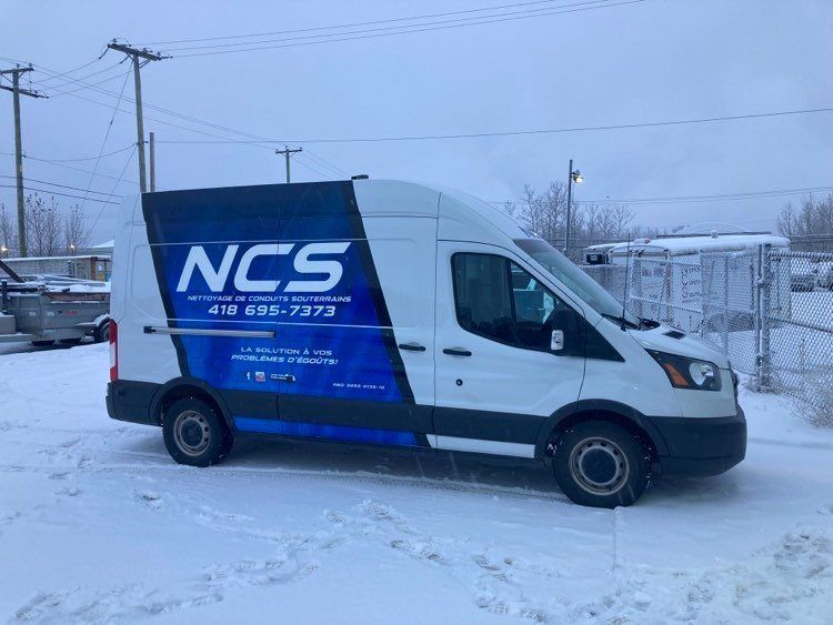 Une camionnette blanche avec le mot NCS sur le côté est garée dans la neige.