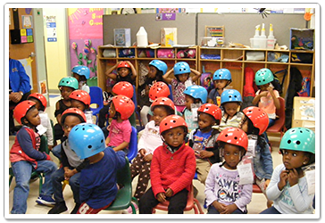Children wearing colorful helmets sit in a classroom.