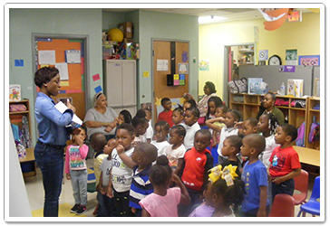 Teacher reading to a group of children in a colorful classroom setting.