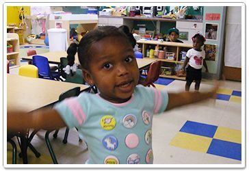 Child with arms outstretched in a colorful preschool classroom.