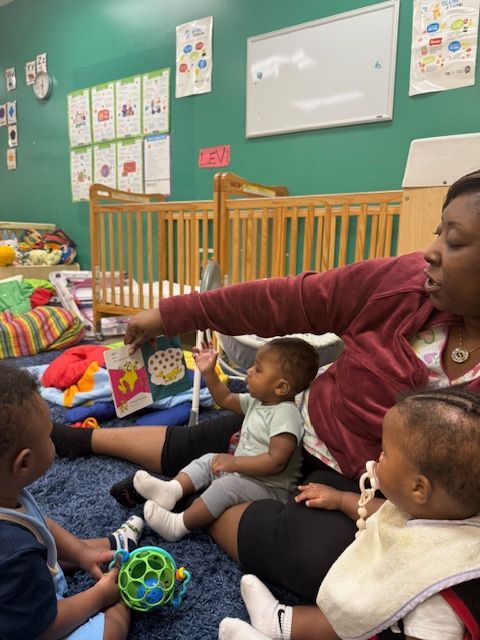 Woman reads to children in a childcare center. Children sit on the floor, some with toys.