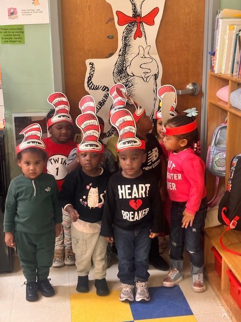 Group of children in matching white shirts; smiles, classroom setting.