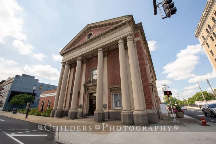 Red brick building with white columns and a triangular pediment. Blue sky with clouds.