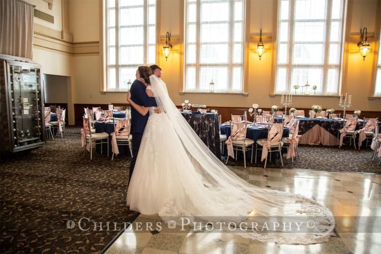 Bride and groom dancing at wedding reception; long veil on marble floor; tables with pink and blue decor.